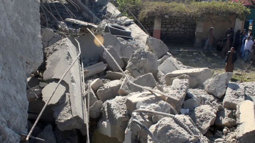People stand in front of a damaged house that the Afghan Taliban government said was damaged after Pakistan carried out raids, in Asadabad, Kunar province, Afghanistan, November 25, 2025/ Reuters