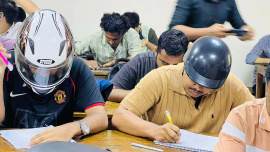 ছাদ থেকে খসে পড়ে পলেস্তারা, তাই হেলমেট পরে পরীক্ষা দিচ্ছেন শিক্ষার্থীরা। ছবি: স্টার